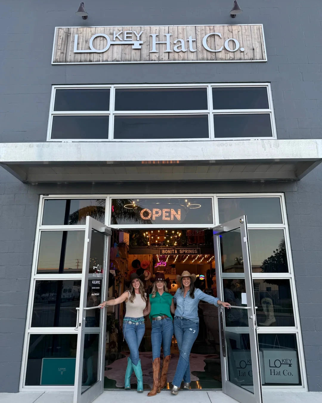 Three women standing in the open door of a building with 'Lokey Hat Co' signage.